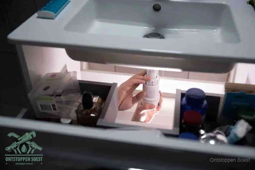 Een pompfles met zeep boven een wastafel, de heet water en afwasmiddel-methode om een vetprop in de afvoer los te maken in Soest
