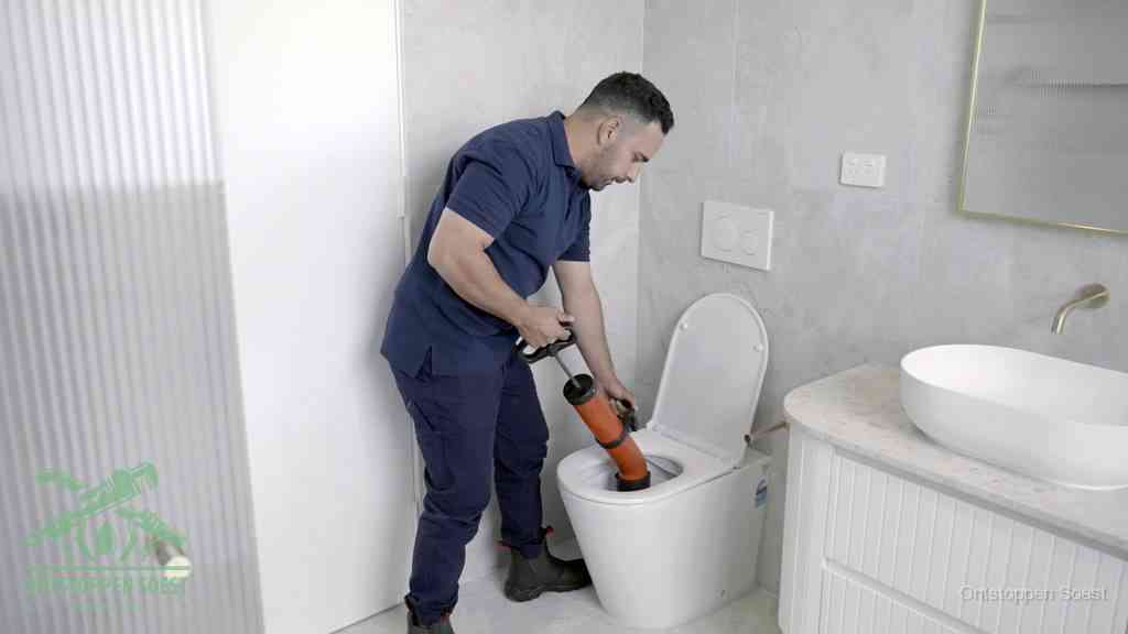 Een monteur buigt over een wandcloset en duwt met de hand een persluchtontstopper in de toiletpot om de verstopping handmatig los te maken in Soest