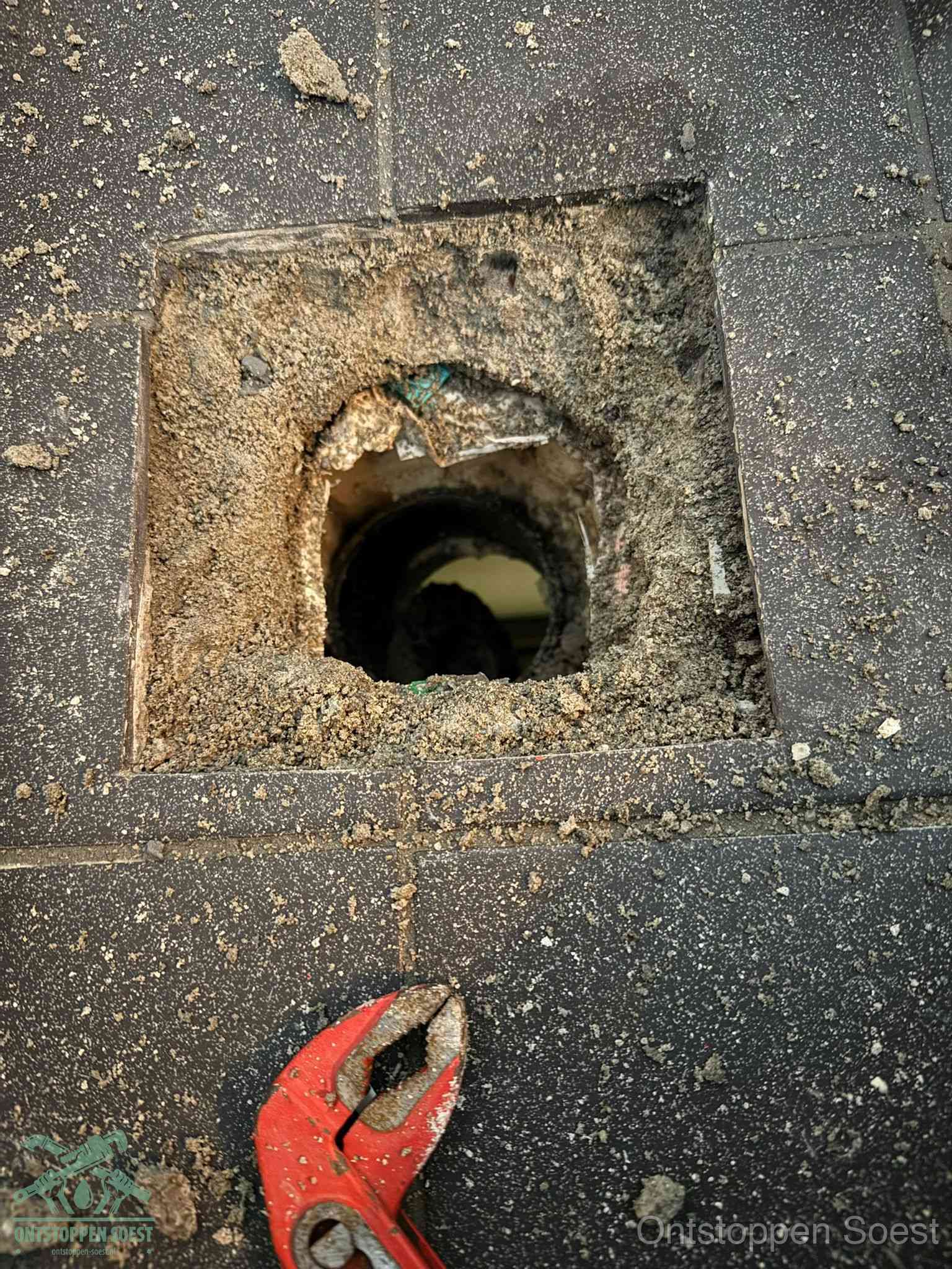 Een geopend rioolputje in een betontegelvloer met losgemaakt rooster en een zichtbare ronde afvoerbuis, het achterhalen waar de afvoerverstopping zit in Soest