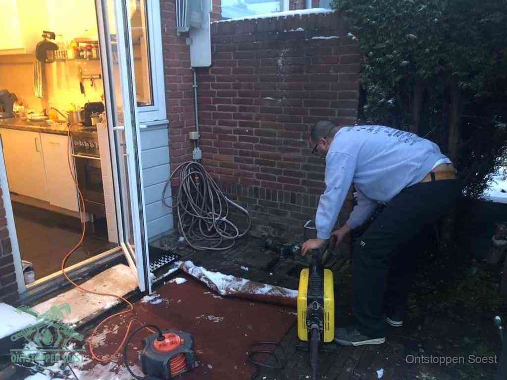 Een monteur werkt buiten bij een open riool-/grondput met een elektrische ontstoppingsmachine om een verborgen afvoerprobleem op te sporen in Soest