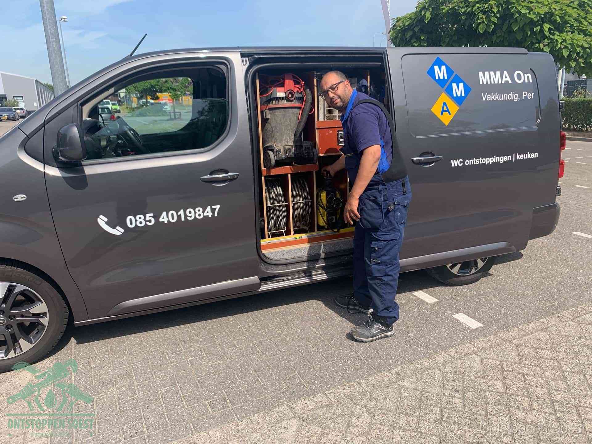 Een monteur bij de open schuifdeur van zijn bedrijfsbus op een parkeerplaats, klaar om de oorzaak van terugkerende afvoerverstoppingen aan te pakken in Soest