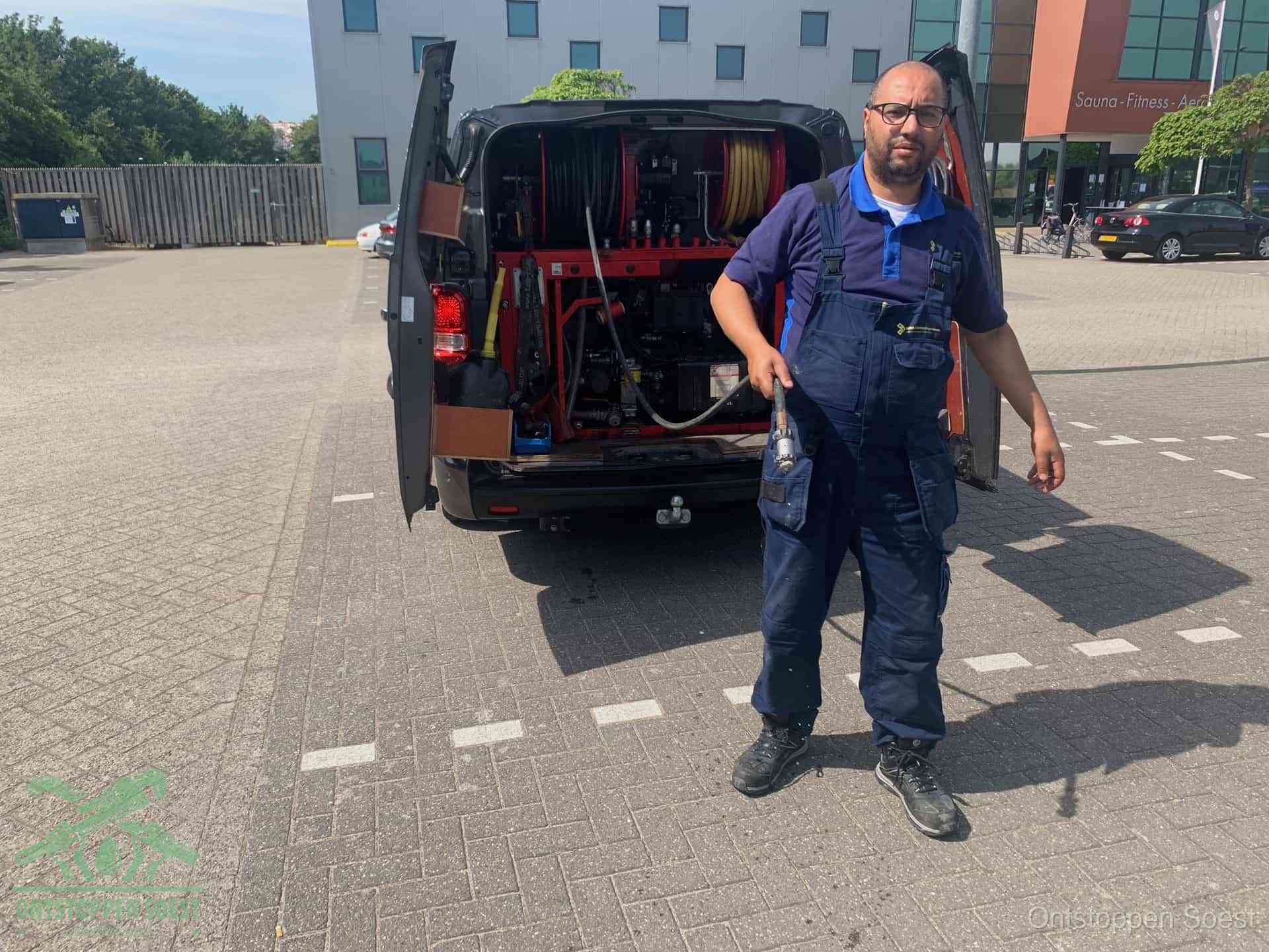 Een monteur bij zijn bestelbus met een hogedruk- en rioolreinigingsunit, klaar om de oorzaak van terugkerende wc-verstoppingen aan te pakken in Soest